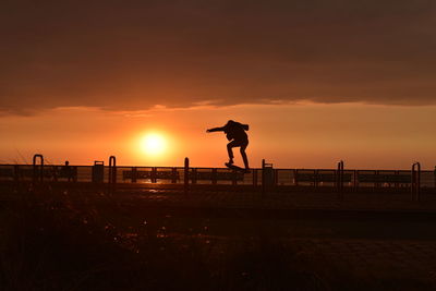 Silhouette man skating on boulevard against sky during sunset