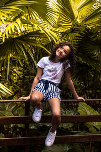 Full length of girl sitting on railing against trees