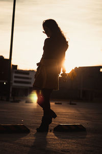 Side view of woman standing on street at sunset