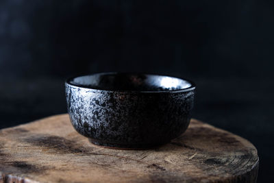 Close-up of black bowl on tree stump against black background