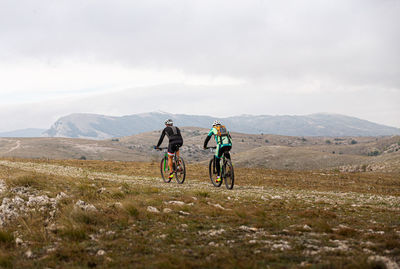 People riding bicycle on mountain against sky