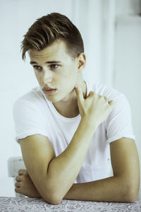 Thoughtful young man looking away while sitting against wall