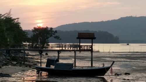 Boat moored on beach against sky during sunset