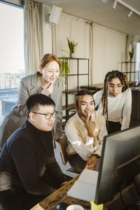 Multiracial male and female programmers discussing over computer at desk in creative office