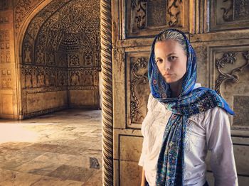 Portrait of young woman standing against wall