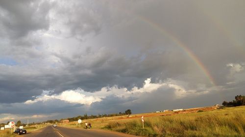 Road passing through field against cloudy sky