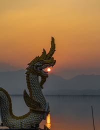 Statue by lake against sky during sunset