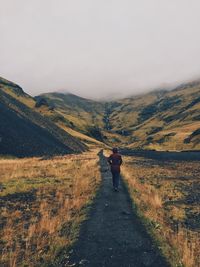 Rear view of woman walking on trail leading towards mountains