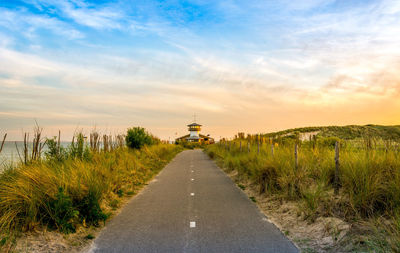 Road leading towards amidst field against sky