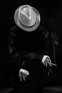 Rear view of person wearing hat standing against black background