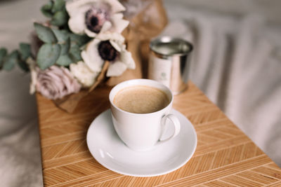 Coffee cup on table on bed, flowers and candles. eucalyptus and anemones. interior gray tones