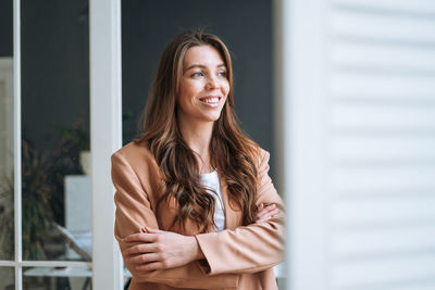 Young business woman with dark long hair in stylish beige suit near window in the modern office