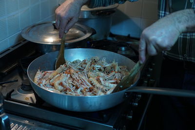 Midsection of man cooking shrimps in pan at kitchen