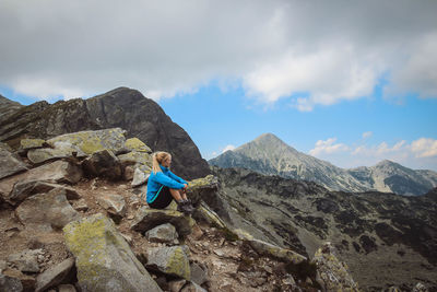 Woman sitting on rock by mountains against sky