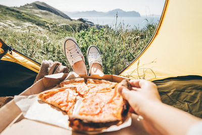 Woman eating takeaway pizza at the camping tent at the mountain.