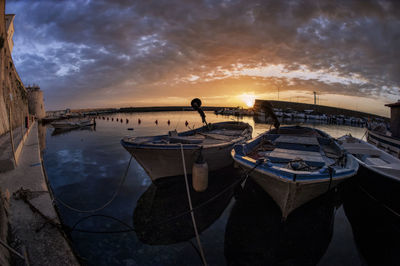 Boats moored in sea against sky during sunset