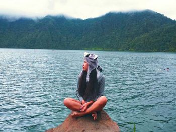 Young woman relaxing on rock at lake during foggy weather