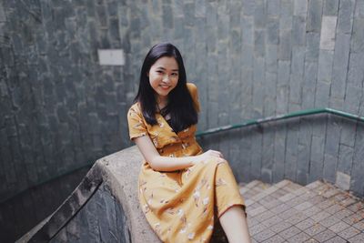 Portrait of smiling woman sitting against wall