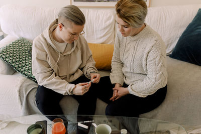 Lesbian couple looking at ivf syringe while sitting on sofa at home