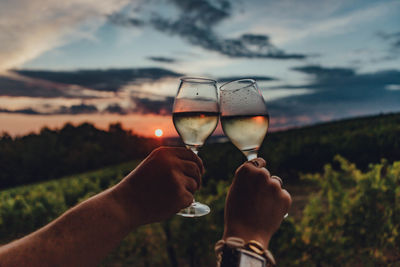 Midsection of man holding wineglass against sky during sunset