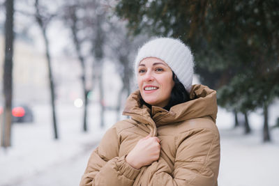 A happy woman in a white hat is warming herself in a coat. it stands in the city in winter