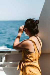 Rear view of woman standing by sea against sky