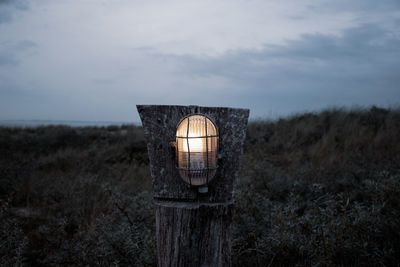 Illuminated lamp on field against sky at dusk