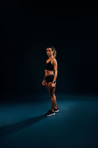 Portrait of young woman standing against black background