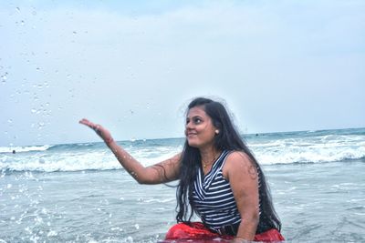 Portrait of beautiful young woman on sea shore against sky