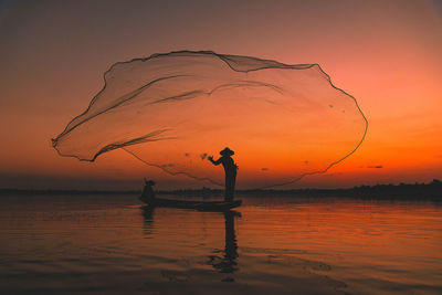 Silhouette people fishing in sea against sky during sunset