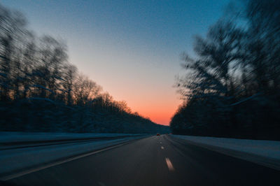 Road by trees against sky during sunset