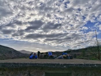 People relaxing on land against sky