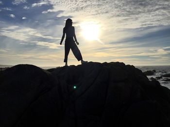 Silhouette woman standing on rock against sea during sunset