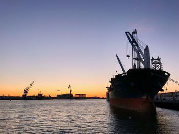 Silhouette cranes at commercial dock against clear sky