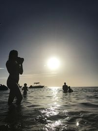 Silhouette men standing on sea against sky during sunset