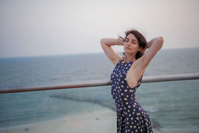 Young woman standing by sea against sky