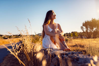 Young woman sitting on field against sky