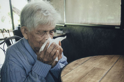 Old person coughing covering mouth with a tissue on a house interior. she has flu, allergy symptoms.