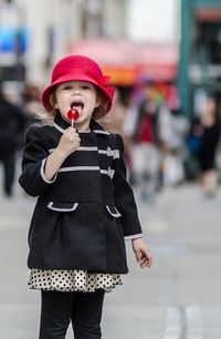 Portrait of girl eating lollipop while standing on street in city