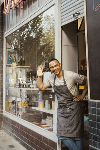 Happy male owner waving while standing at store doorway