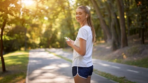 Full length of young woman holding smart phone while standing outdoors