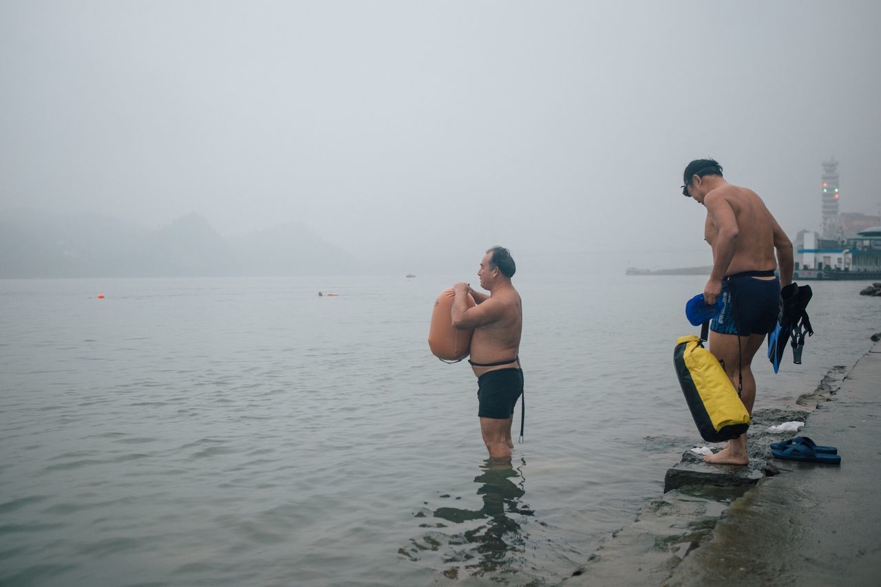 water, sea, tranquil scene, scenics, men, waterfront, full length, togetherness, tranquility, beauty in nature, casual clothing, nature, sky, day, remote, vacations, in front of, non-urban scene