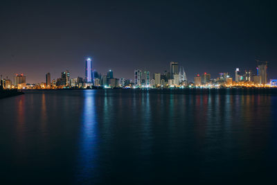 Illuminated buildings by river against sky at night