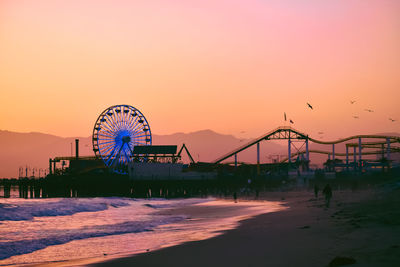 Low angle view of amusement park against sky during sunset