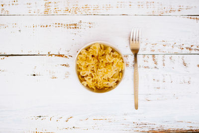 Classic homemade macaroni and cheddar cheese on black plate with a fork on white wooden table.