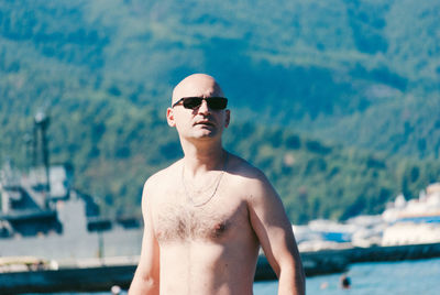 Shirtless bald man wearing sunglasses against mountain