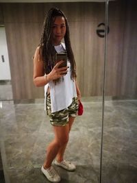 Full length of young woman using phone while standing on mirror