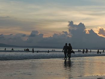 Silhouette people at beach against sky during sunset