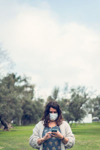 Woman wearing mask using smart phone standing at park