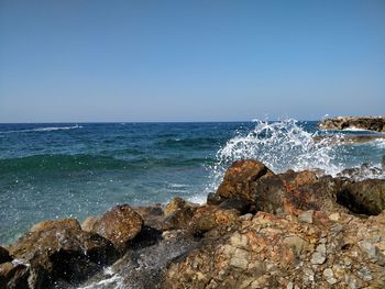 Sea waves splashing on rocks against clear sky